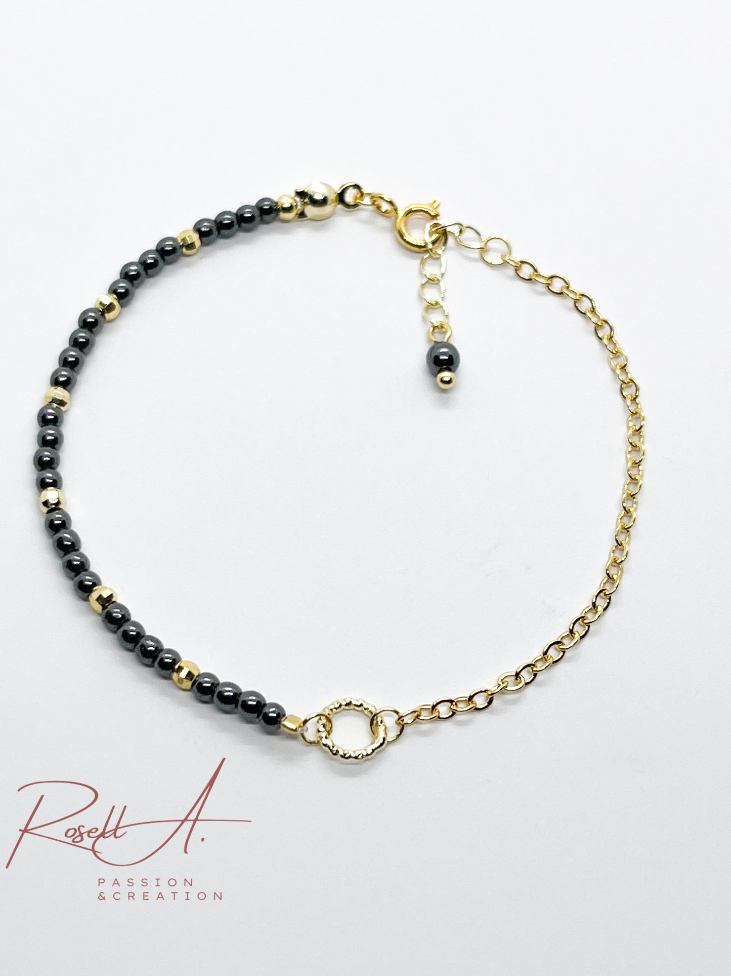 Draufsicht des filigranen, asymmetrischen Armbands mit Hämatitperlen, geriffeltem Ring und vergoldeter Ankerkette.